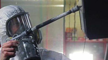 Koruyucu giysili işçiler metal yüzeye boya püskürtüyor, hava tabancası ve güvenlik maskesi ile sanayi boyama işlemi yapıyor..