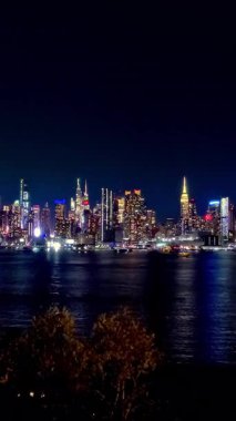 Zaman aşımına uğramış New York şehrinin ufuk çizgisi gece vakti su üzerindeki yansımalarla aydınlanıyor, New York City 'nin nefes kesen gece manzarası.