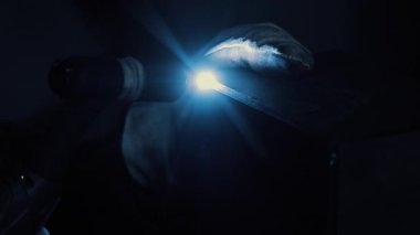 Kaynakçı parlak ark ışığı ile TIG kaynaklama yapıyor, karanlık atölye ortamında metal birleştiren eldivenli ellerin yakın çekimi.