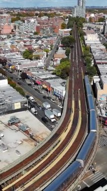 Şehir Rayları ve Şehir Manzarası Hava Görüntüsü. Yükseltilmiş tren rayları yoğun binalar, işlek caddeler ve şehir altyapısı olan kalabalık bir şehir mahallesi boyunca kıvrımlı bir viraj oluşturuyor.
