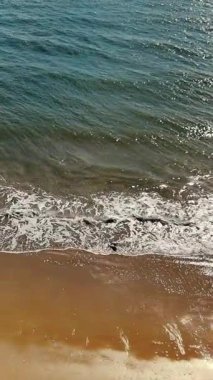 Dalgalar yavaşça kumsala ulaşıyor. Kumlu kıyı şeridinde süzülen küçük dalgaların yakın görüntüsü, parlak güneş ışığı altında ışıldayan su huzur verici bir sahne yaratır.