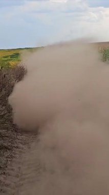 Toprak yolda toz kaldıran araba, toprak yolda hız yapan beyaz araba, mısır tarlaları ve güneş ışığıyla çevrili büyük bir toz bulutu oluşturuyor..