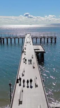 Manzaralı Okyanus İskelesi 'nde güneşli bir gün. Işıl ışıl okyanusa doğru uzanan parlak mavi gökyüzünün altında insanların gezindiği ve rahatladığı bir iskelenin havadan görünüşü.