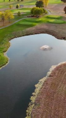 Manzaralı Golf Sahası Göleti 'nin havadan görünüşü, yemyeşil çayırları olan bir golf sahasının insansız hava aracı görüntüsü, fıskiyeli sakin bir gölet ve çevre yolları..