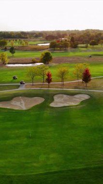 Güz Ağaçlı Manzaralı Golf Sahası, Kum tuzaklarının, canlı sonbahar ağaçlarının, göletlerin ve yumuşak güneş ışığı altında yeşil çayırların bulunduğu yemyeşil bir golf sahasının havadan görünüşü.