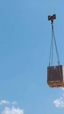İnşaat alanındaki tuğla paletini kaldıran bir vinç inşaat alanındaki tuğla paletini havaya kaldıran bir vinç bulutlu açık mavi bir gökyüzüne karşı kurulmuş..