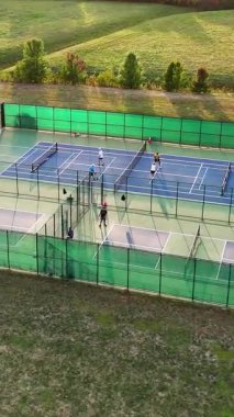 Açık Tenis ve Pickleball sahalarının hava görüntüsü. Yeşil alanlar ve ağaçlarla çevrili oyunların keyfini çıkaran oyuncularla çitle çevrili açık hava tenis ve yankesicilik sahaları.