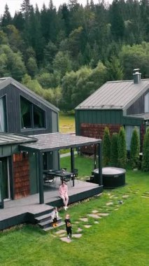 Dağlarda eğlence için modern ahşap evler. Evin yakınında iki küçük çocuğu olan bir anne. Koyu renkli ahşap kaplamalı iki modern kulübe..