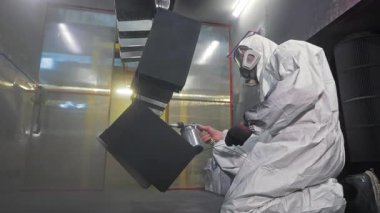 Koruyucu kıyafetli bir ressam, metal parçaları standa püskürtüyor, endüstriyel kaplama işlemi yapıyor. Aşınma direnci ve yüzey dayanıklılığı için pudra önlüğü uygulaması.