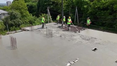 Construction Workers Pouring Concrete Slab On Rooftop Using Pump Hose And Tools, Team In Safety Vests Working On Modern Urban Building Project.