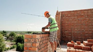 Tuğlacı Üst Katta Duvar Yapıyor İçi boş kil tuğlaları kullanıyor, Açık Gökyüzü Altında Güvenlik Dişlisini Giyiyor.