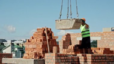 İşçi Rehberi Büyük Beton Konteynır Crane tarafından Sunlight 'taki çatı inşaat sahasında askıya alındı.