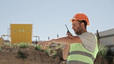 Güvenlik Yeleği ve Miğfer İnşaat Yöneticisi, Çalışma Alanını Gösterirken Telsiz-Telsiz Kullanıyor.