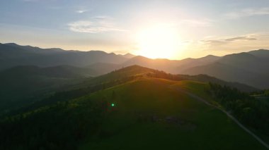 Yeşil yuvarlanan tepeleri ve dağ sırtlarını aydınlatan güneşin doğuşunun havadan görünüşü huzurlu ve manzaralı bir sabah atmosferi yaratıyor.