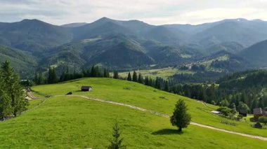 Kırsal kabinleri ve dolambaçlı yolu olan bir dağ çayırı. Dağılmış kulübeleri olan parlak yeşil çayır, kıvrımlı bir toprak yol ve görkemli dağ zirvelerine kurulmuş çam ormanı.