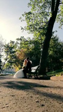 Damat ve gelin parkta bir bankta oturuyorlar. Sonbahar Parkı ve Sabah Güneşi