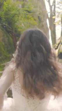 Gelin, altın güneşin altındaki uçurumların arasından koşuyor. Beyaz elbisesi arka planda parlıyor ve kameraya doğru gülümserken yüzünde neşeli bir enerji parlıyor..