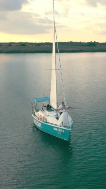 Ukrayna. Lviv. 19.09.2020. Altın gün batımında yatın insansız hava aracı görüntüsü. Aşağıdaki sakin deniz, beyaz yelkenin yanından geçen güneş ve bulutları yansıtıyor..