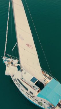 Gün batımında bir yat açık denizde yelken açar. Parlayan gökyüzünün yansıması ve suyun üzerindeki bulutlar sakin ve romantik bir kaçış atmosferi yaratır..