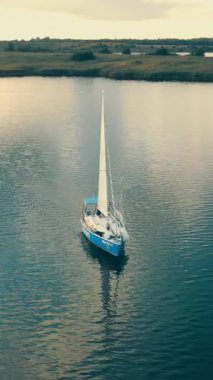 Ukrayna. Lviv. 19.09.2020. Gün batımında tek bir yatın havadan görüntüsü. Su, teknenin yanında uçan insansız hava aracı gibi gökyüzünü yansıtıyor. Altın ışıkta beyaz yelkenini gösteriyor..