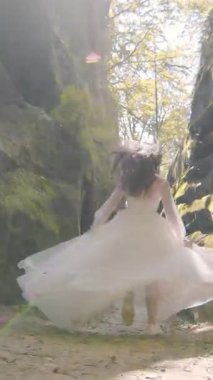 Gelin sevinçle kameraya doğru koşuyor, kayalık manzarayla çerçevelenmiş. Gelinliği, arkasında güneş parıldarken süzülüyor. Anı yumuşak altınla aydınlatıyor..