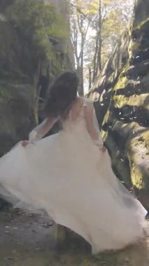 Beyaz gelinlik giymiş gelin kayaların arasından gülümsüyor. Arkasındaki güneş ışığı çarpıcı parlaklıklar yaratır ve altın bir parıltıyla örtüsünü aydınlatır..