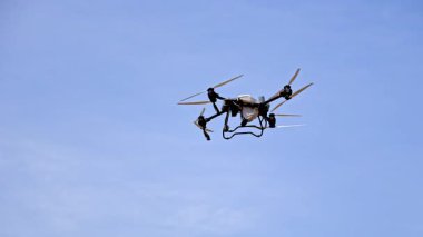 Mavi gökyüzünde uçan hava tarımsal dronu. Tarım ve ekin izleme görevleri için kullanılan, açık mavi gökyüzüne karşı uçan bir sprey sistemi ile donatılmış kuadkopter drone