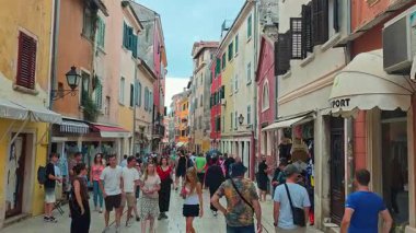 Rovinj, Hırvatistan. 20 Ağustos 2025: Renkli kepenkli binalar ve canlı yerel yaşam tarzını yakalayan mağaza tenteleri arasında yayalar ile dolu eski Avrupa kasabası sokağı.