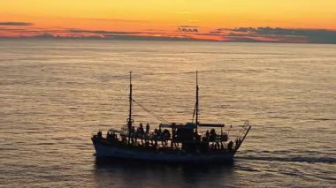 Adriyatik Denizi 'nde gün batımında seyreden turist teknesi altın ufuk çizgisine karşı siluetlenmiş yolcularla birlikte..