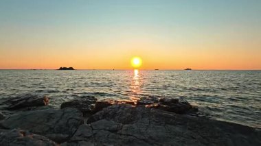 Sakin Adriyatik Denizi üzerinde altın gün batımı parlayan ufuk ve kayalık kıyı önplanıyla, huzurlu deniz manzarası doğa güzelliğini ve kıyı akşam dinginliğini temsil ediyor..