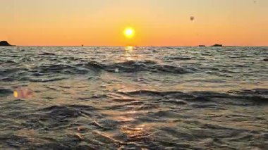 Yumuşak deniz dalgalarının üzerinde gün batımı, altın ışığı yansıtan, sıcak tonlarda parlayan, doğanın güzelliğini ve yaz akşamının sükunetini simgeleyen manzaralı deniz manzarası..
