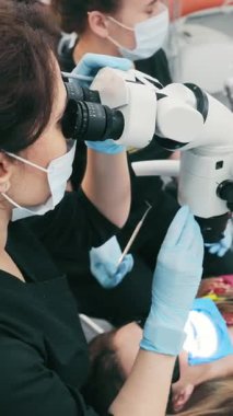 Diş hekimi ve asistanı bir mikroskop kullanarak hastayı muayene ediyorlar. Bir doktor mikroskopla bakar. Modern diş sağlığı kliniği.