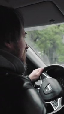 Ellerini kullanmadan araba kullanan bir adam. Deri ceketli bir adam, ağaçlı bir caddenin ön paneline bağlanmış, elleri boş bir telefonla konuşurken araba kullanıyor.