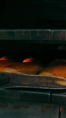 Fırıncı ekmeği fırından büyük tahta bir kürekle çıkarır, yakın plan. Fırın işi. Ekmek ve fırın ürünleri pişirmek