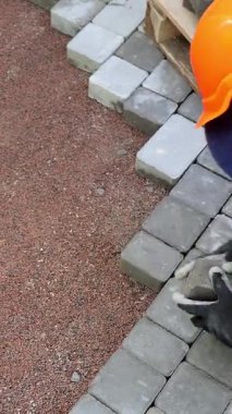 İşçi Pavement Blokları, turuncu güvenlik teçhizatı içinde bir işçi dikkatle birbirine kenetlenmiş kaldırım bloklarını yeni hazırlanmış taban tabakasına yerleştiriyor.