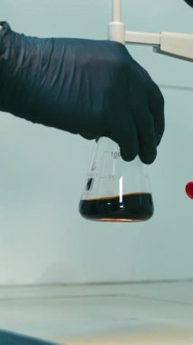 Bilimadamı, bir kimya laboratuvarında, mataradan mataraya madde döküyor.