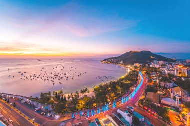 Vung Tau city aerial view with beautiful sunset and so many boats. Panoramic coastal Vung Tau view from above, with waves, coastline, streets, coconut trees and Tao Phung mountain in Vietnam.
