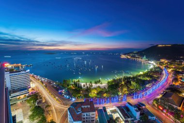 Vung Tau city aerial view with beautiful sunset and so many boats. Panoramic coastal Vung Tau view from above, with waves, coastline, streets, coconut trees and Tao Phung mountain in Vietnam.