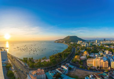 Vung Tau city aerial view with beautiful sunset and so many boats. Panoramic coastal Vung Tau view from above, with waves, coastline, streets, coconut trees and Tao Phung mountain in Vietnam.