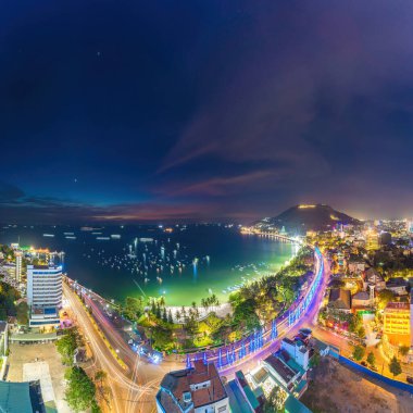 Vung Tau city aerial view with beautiful sunset and so many boats. Panoramic coastal Vung Tau view from above, with waves, coastline, streets, coconut trees and Tao Phung mountain in Vietnam.