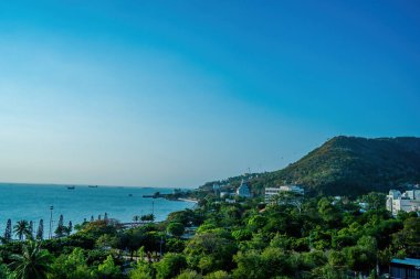 Vung Tau city aerial view with beautiful sunset and so many boats. Panoramic coastal Vung Tau view from above, with waves, coastline, streets, coconut trees and Tao Phung mountain in Vietnam.