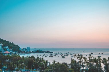 Vung Tau city aerial view with beautiful sunset and so many boats. Panoramic coastal Vung Tau view from above, with waves, coastline, streets, coconut trees and Tao Phung mountain in Vietnam.