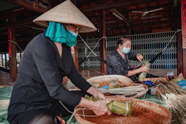 Vung Tau, VIETNAM - JAN 23 2022: Focus old woman with traditional Vietnamese dress (ao ba ba) Making (wrapping) Tet Cake, the Vietnamese lunar new year Tet food outdoor by hands.