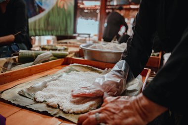 Focus old woman with traditional Vietnamese dress (ao ba ba) Making (wrapping) Tet Cake, the Vietnamese lunar new year Tet food outdoor by hands.