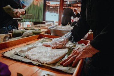 Focus old woman with traditional Vietnamese dress (ao ba ba) Making (wrapping) Tet Cake, the Vietnamese lunar new year Tet food outdoor by hands.
