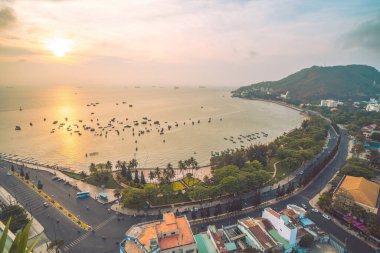 Vung Tau city aerial view with beautiful sunset and so many boats. Panoramic coastal Vung Tau view from above, with waves, coastline, streets, coconut trees and Tao Phung mountain in Vietnam.