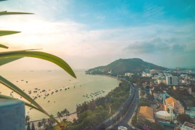 Vung Tau city aerial view with beautiful sunset and so many boats. Panoramic coastal Vung Tau view from above, with waves, coastline, streets, coconut trees and Tao Phung mountain in Vietnam.
