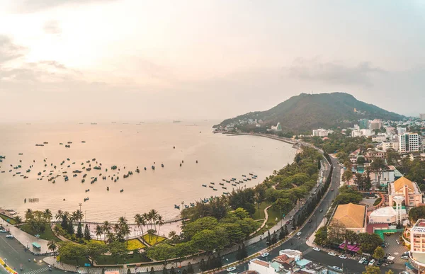 Vung Tau city aerial view with beautiful sunset and so many boats. Panoramic coastal Vung Tau view from above, with waves, coastline, streets, coconut trees and Tao Phung mountain in Vietnam.