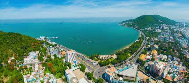 Vung Tau city aerial view with beautiful sunset and so many boats. Panoramic coastal Vung Tau view from above, with waves, coastline, streets, coconut trees and Tao Phung mountain in Vietnam.
