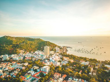 Vung Tau city aerial view with beautiful sunset and so many boats. Panoramic coastal Vung Tau view from above, with waves, coastline, streets, coconut trees and Tao Phung mountain in Vietnam.